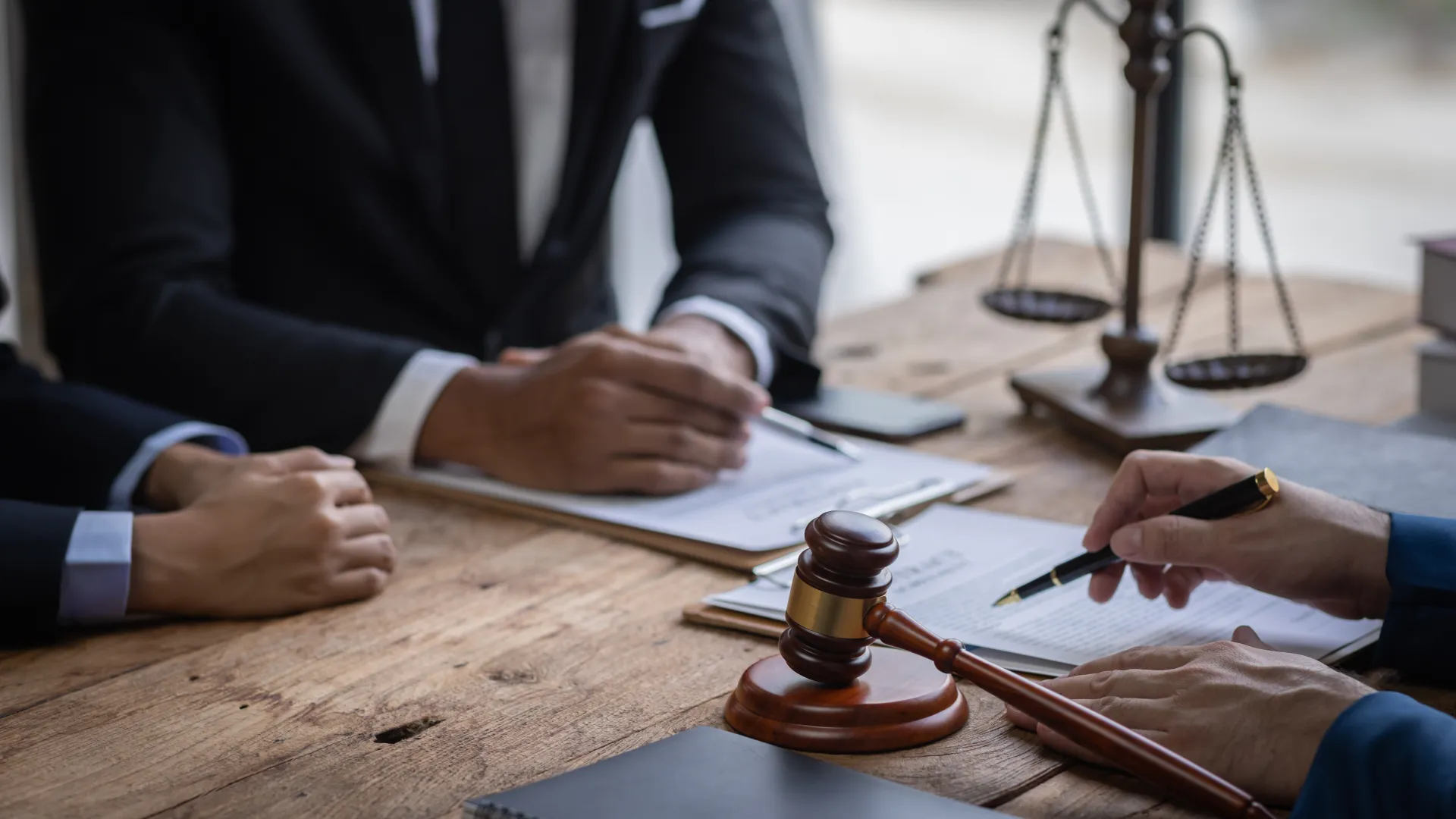 Blick auf einen Schreibtisch, auf dem Verträge liegen, im Hintergrund Justizias Waage